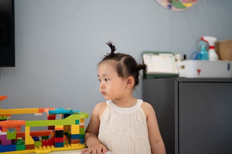 Adorable child with pigtails playing indoors with colorful building blocks.